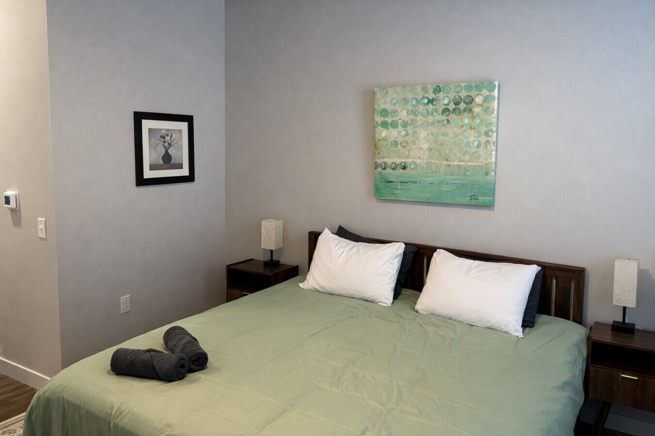 Una camera da letto con un letto, due comodini, un tavolino notte, un quadro incorniciato e un'opera d'arte in mosaico sulla parete.