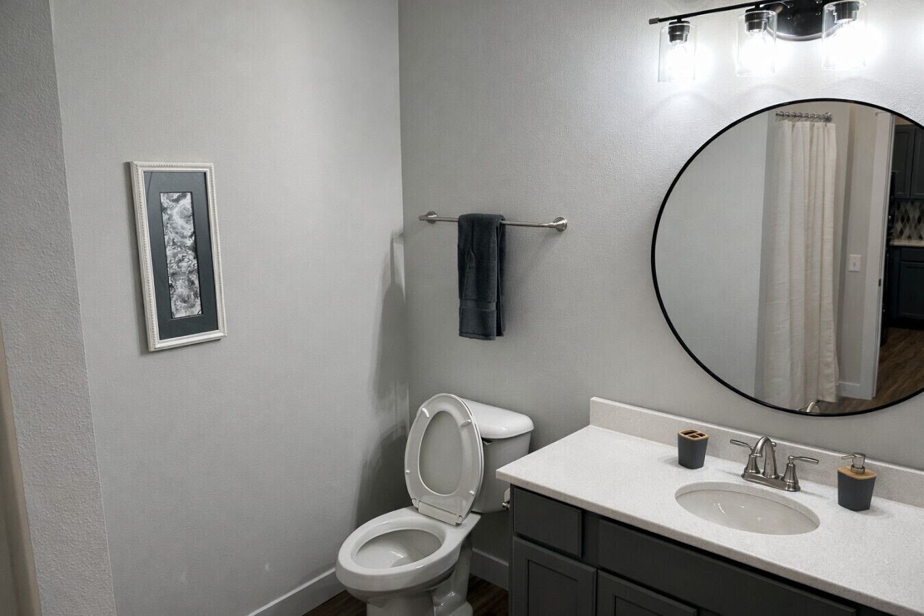 Une salle de bain avec des toilettes, un lavabo, un miroir et un tableau encadré au mur.