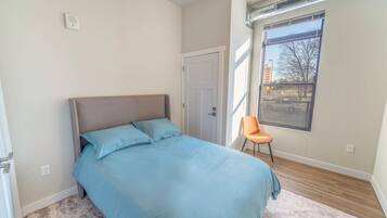 Un dormitorio con cama, una silla, una ventana y una puerta.