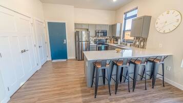 A modern kitchen with stainless steel appliances, a large island with bar stools, and a blue door leading to another room.