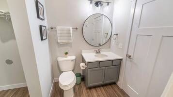 A bathroom with a toilet, sink, mirror, and a towel rack.