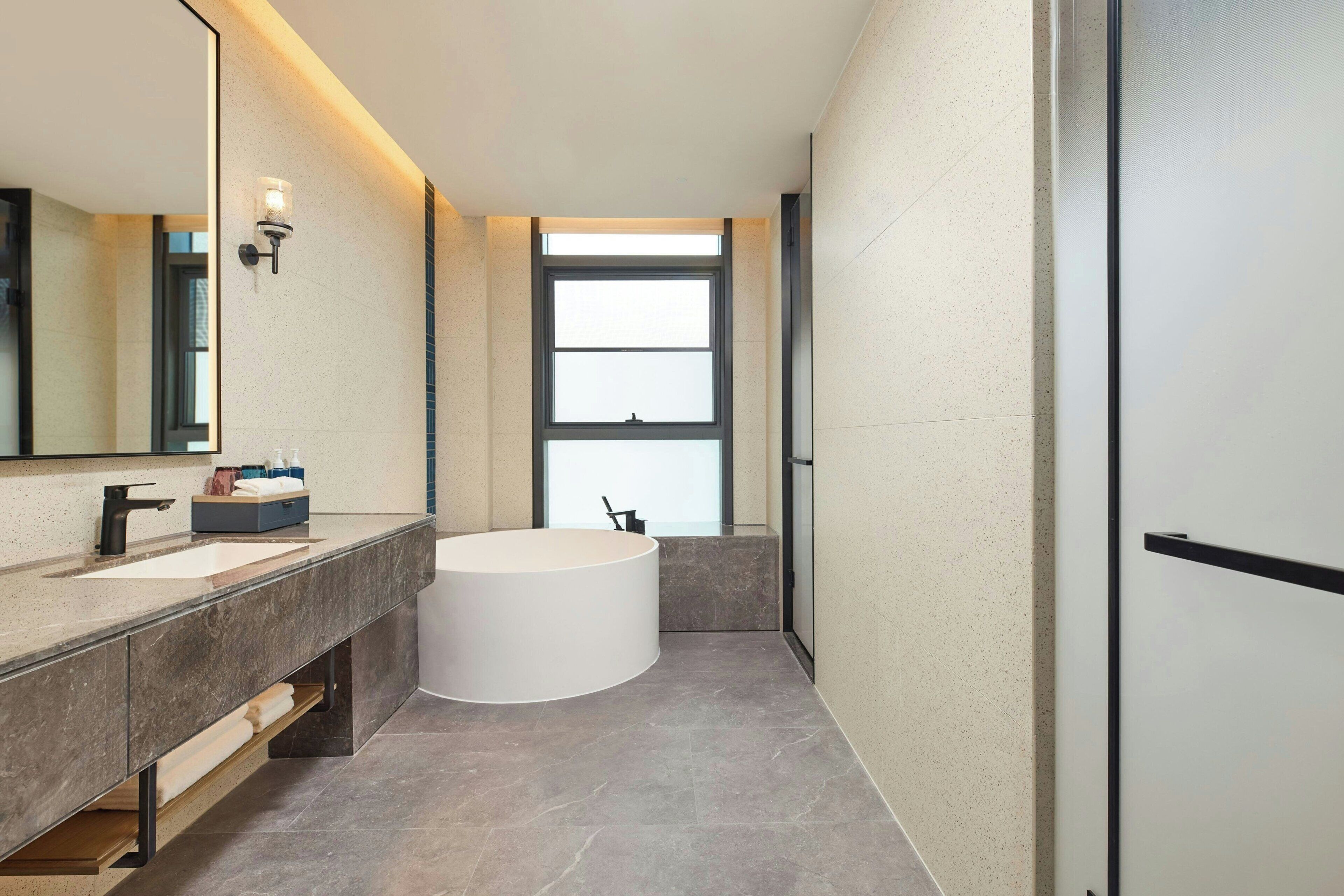 A modern bathroom with a large bathtub, a vanity with a mirror, and a window providing natural light.