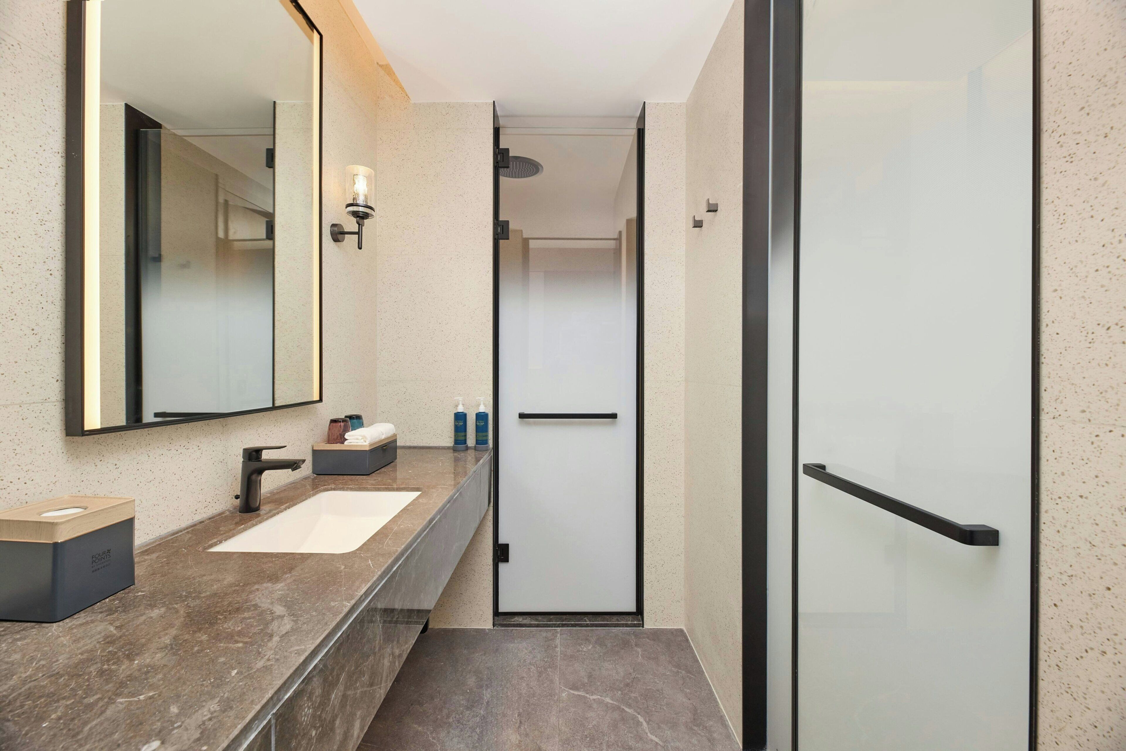Une salle de bain moderne avec un lavabo en marbre, un grand miroir et une cabine de douche en verre.