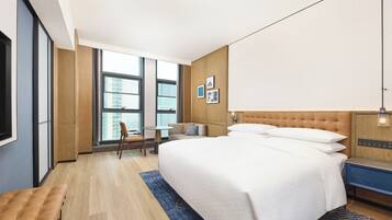 Habitación de hotel moderna con una cama grande, un escritorio, una silla y vistas de la ciudad a través de amplias ventanas.
