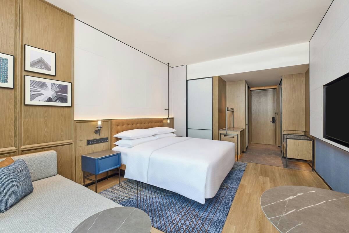 A modern hotel room with a large bed, a sofa, a desk, and a TV.