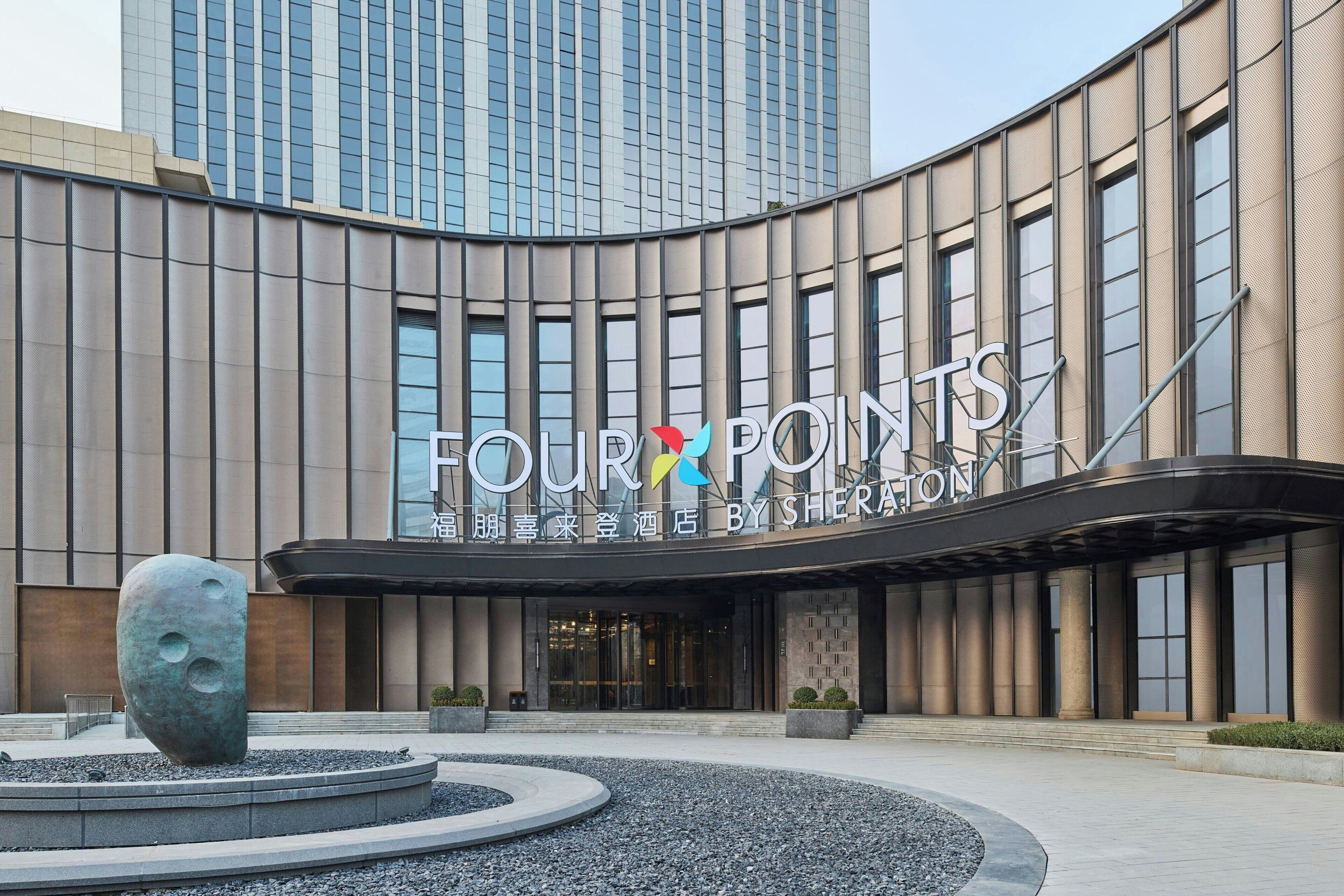 A modern building with a curved facade, a large outdoor sculpture, and the name 'FOUR POINTS BY SHERATON' prominently displayed.