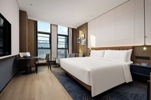 Une chambre d’hôtel moderne dotée d’un grand lit, d’un bureau, d’une chaise, d’une vue sur la ville et d’une grande fenêtre.
