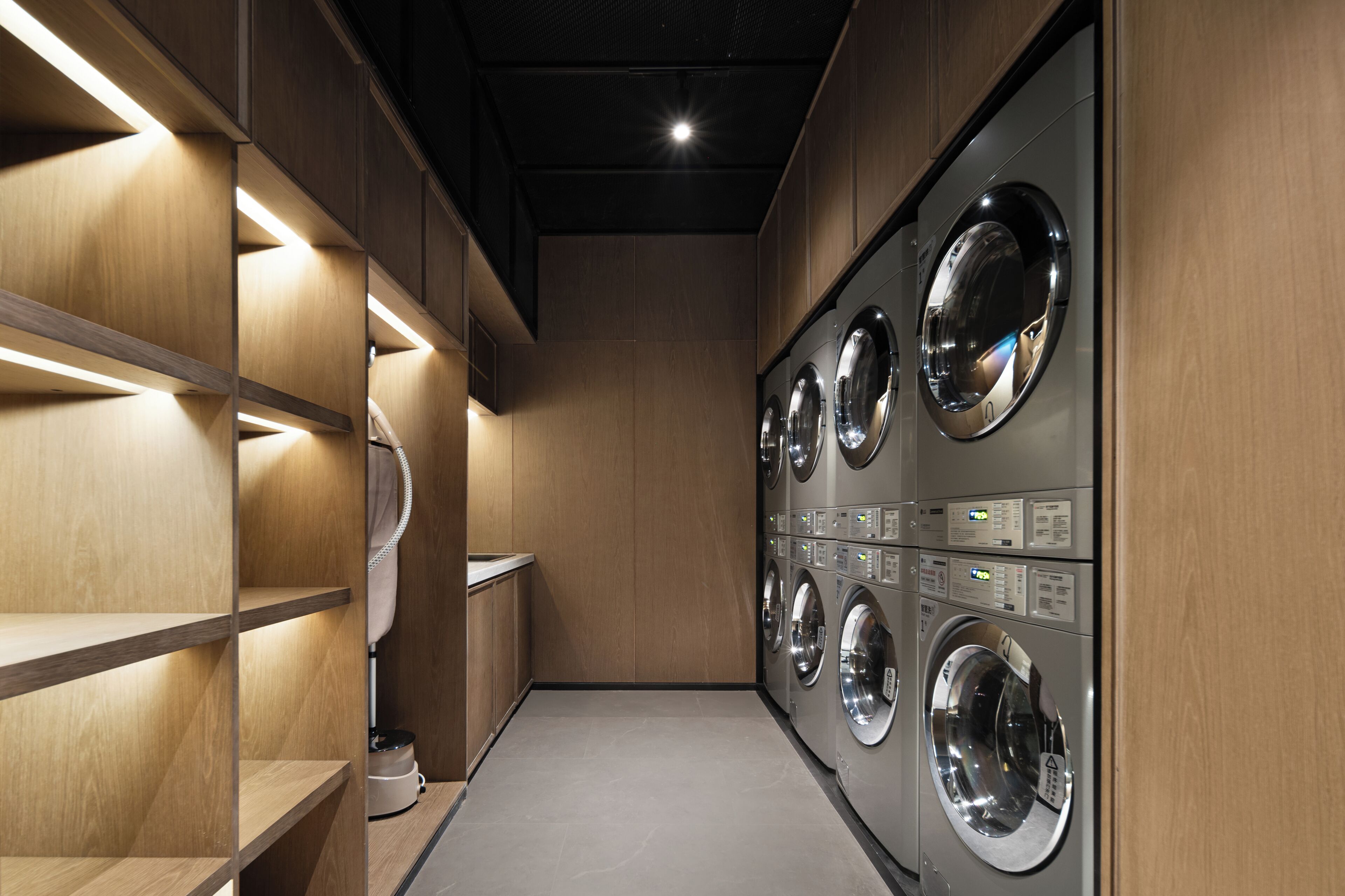A laundry facility with multiple washing machines, wooden shelving, and built-in lighting.