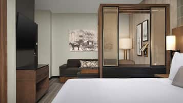 Habitación de hotel con cama, televisor, sofá, mesa de centro, lámpara y un cuadro colgado en la pared.