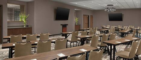Un salón de conferencias con varias mesas y sillas, un espejo grande y dos televisores de pantalla plana montados en las paredes.