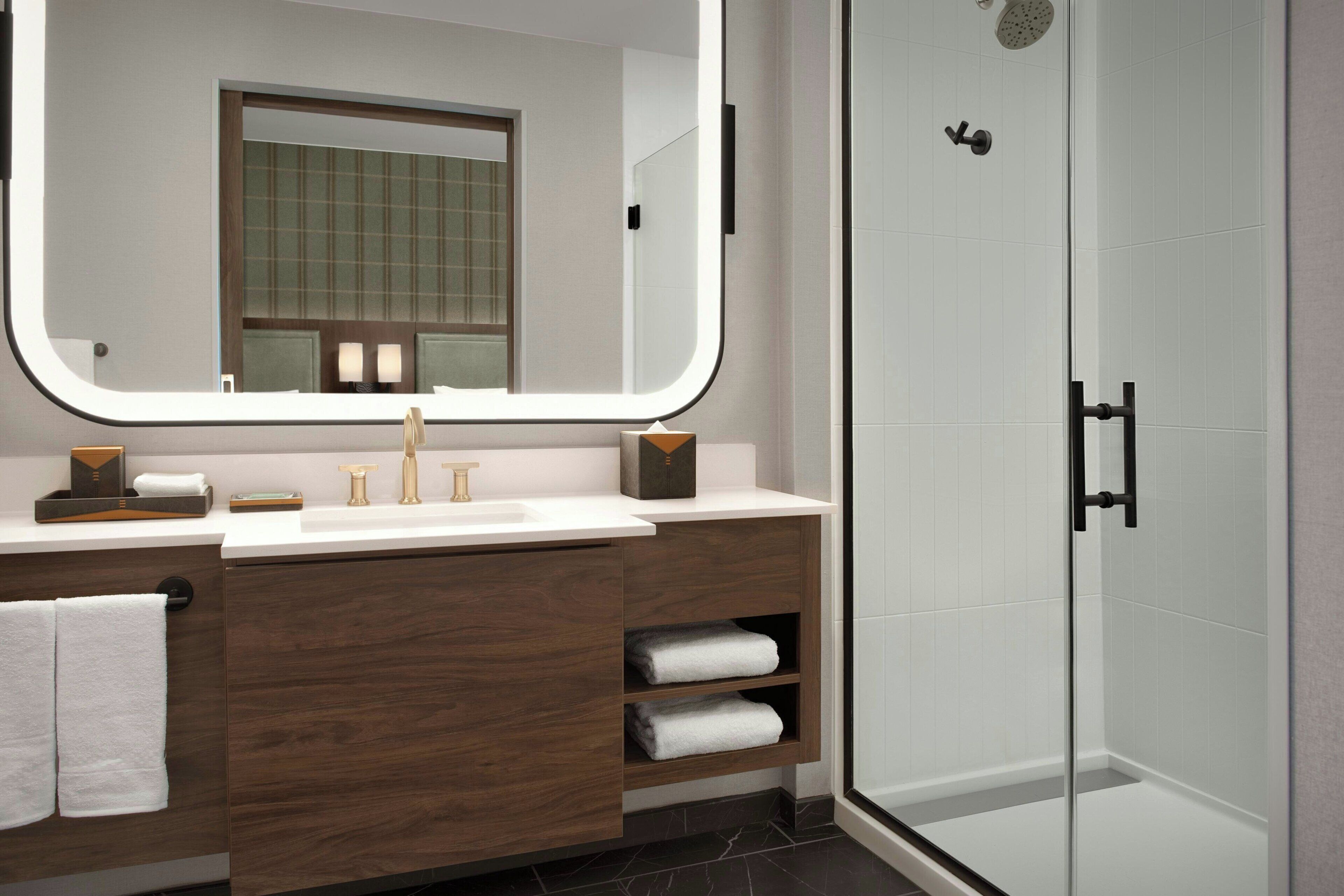 Un baño moderno con un espejo grande, un lavabo, una ducha y un mueble de tocador con espacio de almacenamiento.