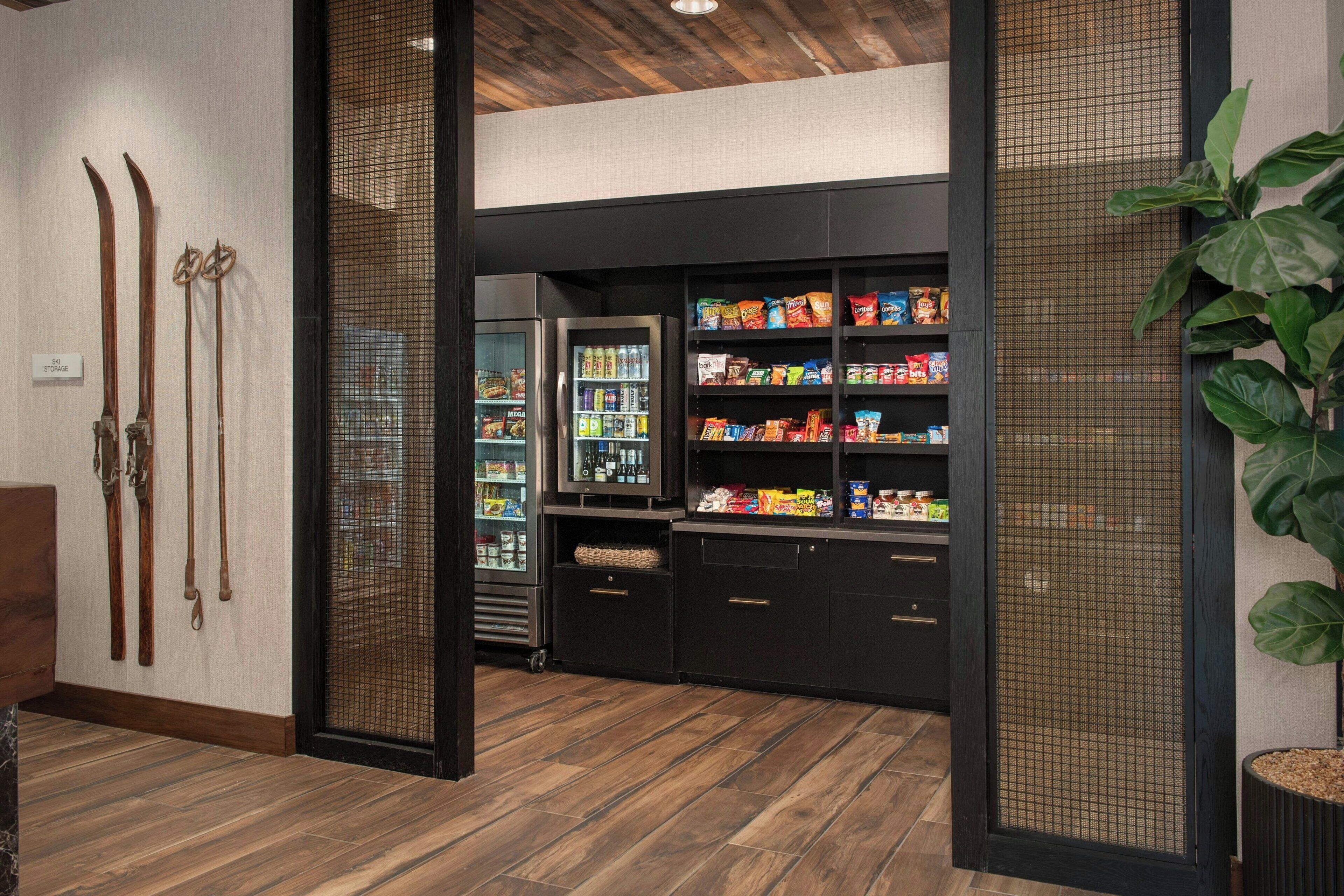 Un vestíbulo de hotel con suelo de madera, zona para guardar esquíes y un bar de aperitivos con diversos productos envasados.