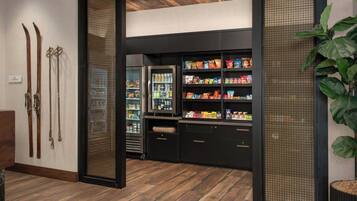Un vestíbulo de hotel con suelo de madera, zona para guardar esquíes y un bar de aperitivos con diversos productos envasados.