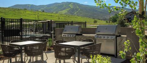 Un patio al aire libre con una parrilla, sillas de mimbre y vistas a una cordillera.