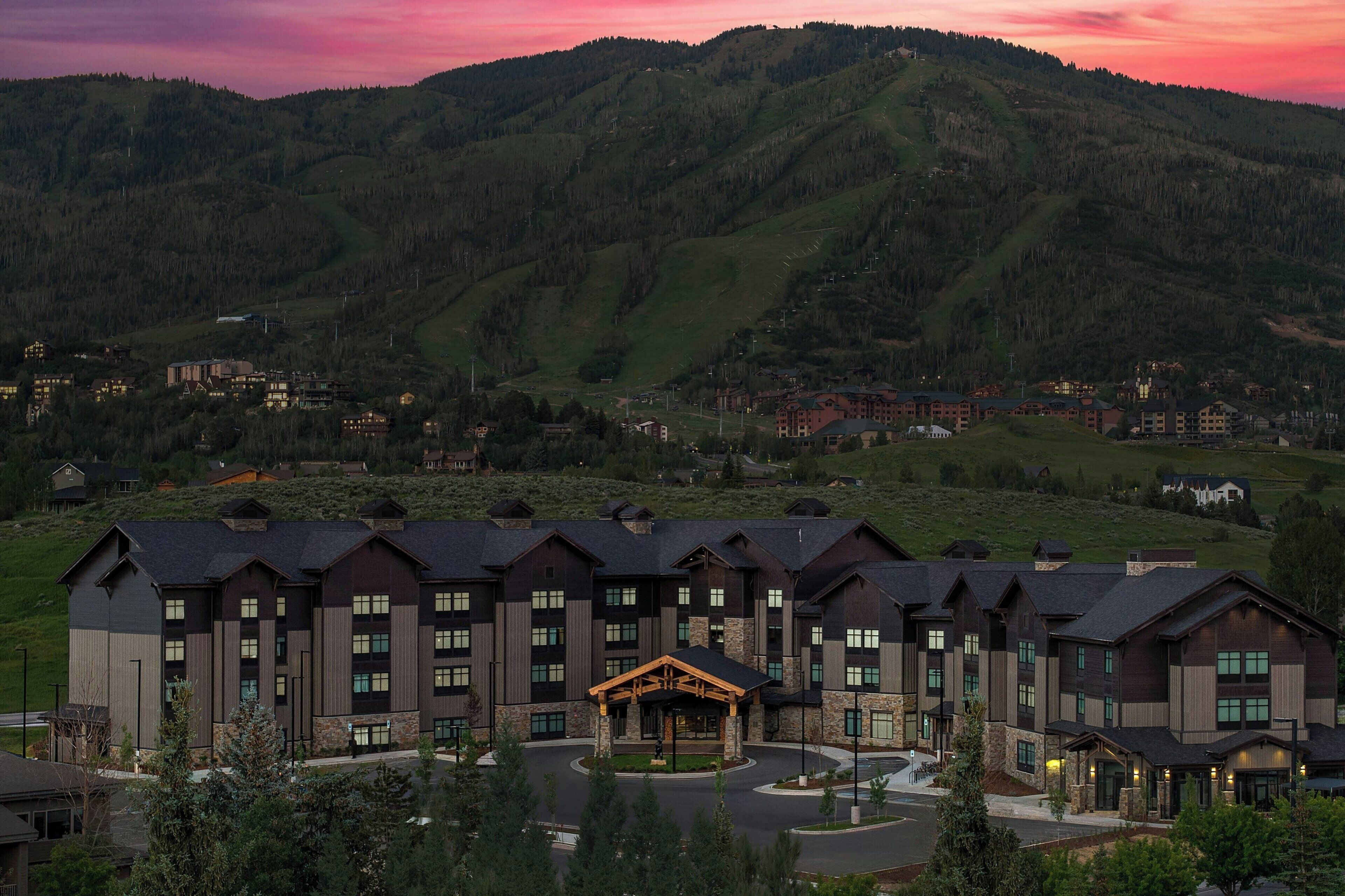Un hotel de varios pisos con un vestíbulo central, rodeado por un paisaje montañoso.