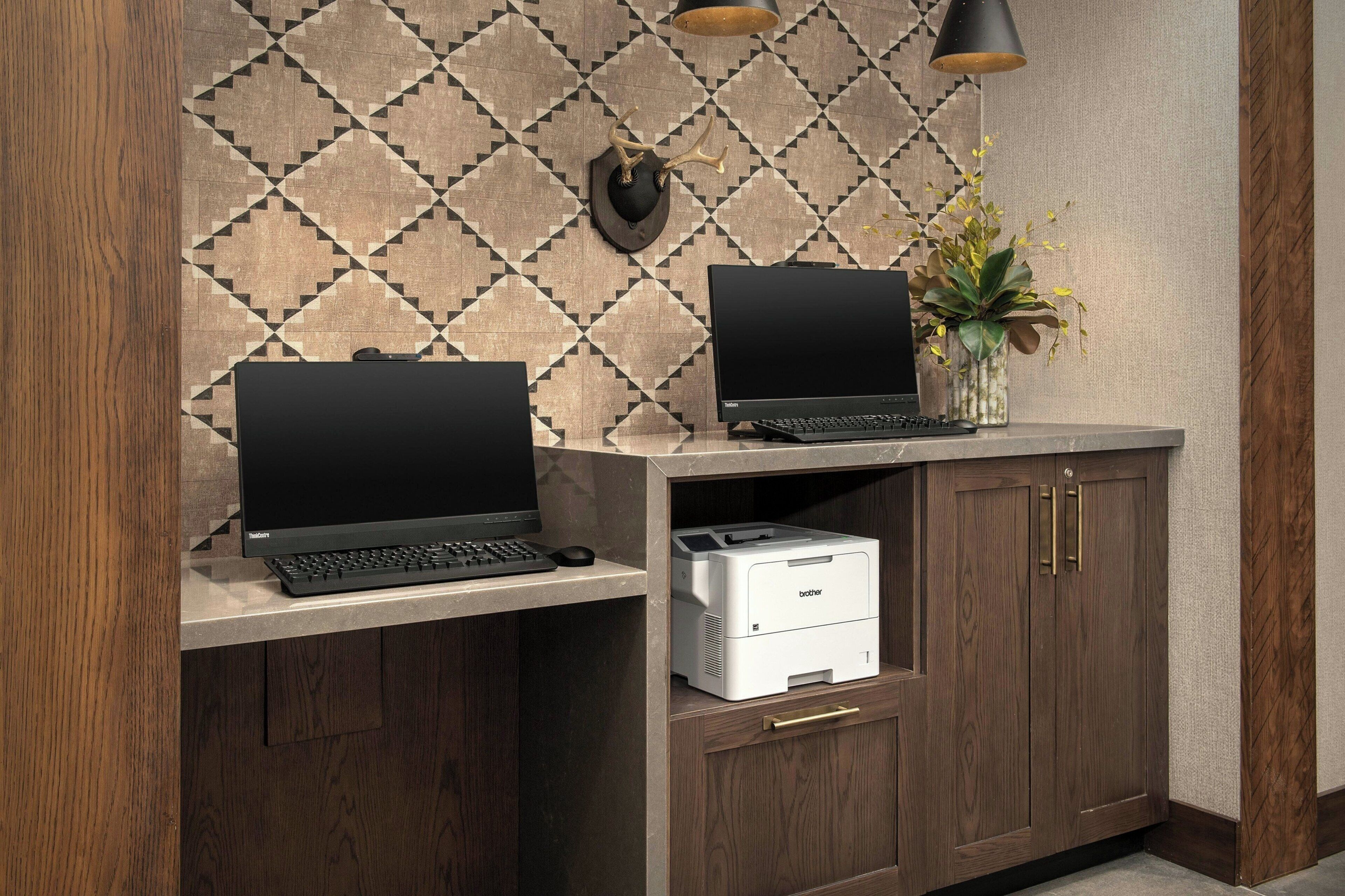 Ein Arbeitsplatz mit zwei Laptops, einem Drucker und einer Wanddekoration.