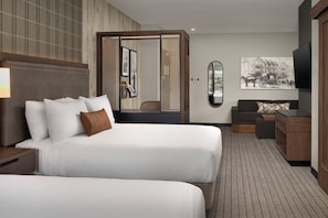 Hotelkamer met twee bedden, een bank, een televisie, een spiegel en een foto aan de muur.