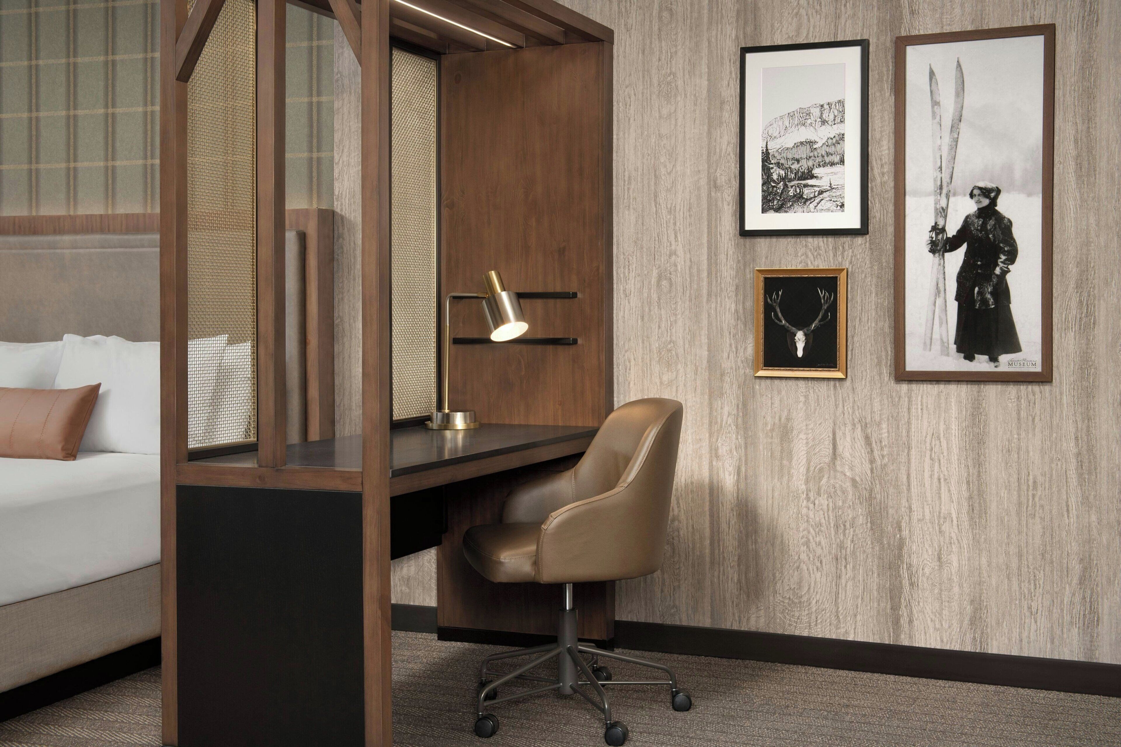 A modern room with a desk, a chair, a bed, and artwork on the wall.