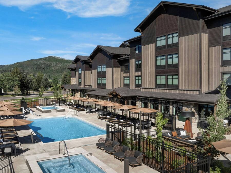 A hotel with a swimming pool, outdoor seating, and a mountainous backdrop.