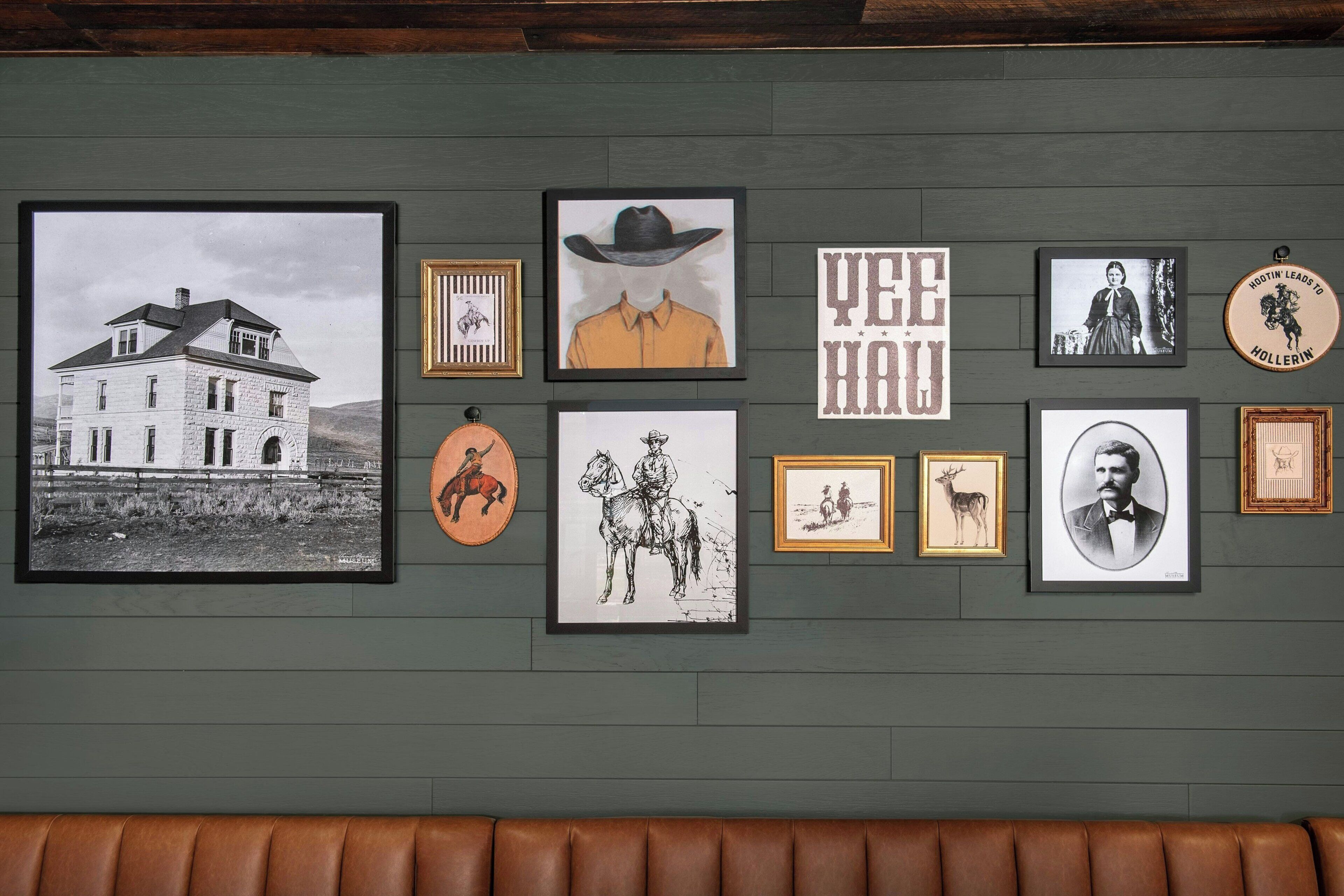 A wall with various framed pictures, including a house, a cowboy, and other historical figures.