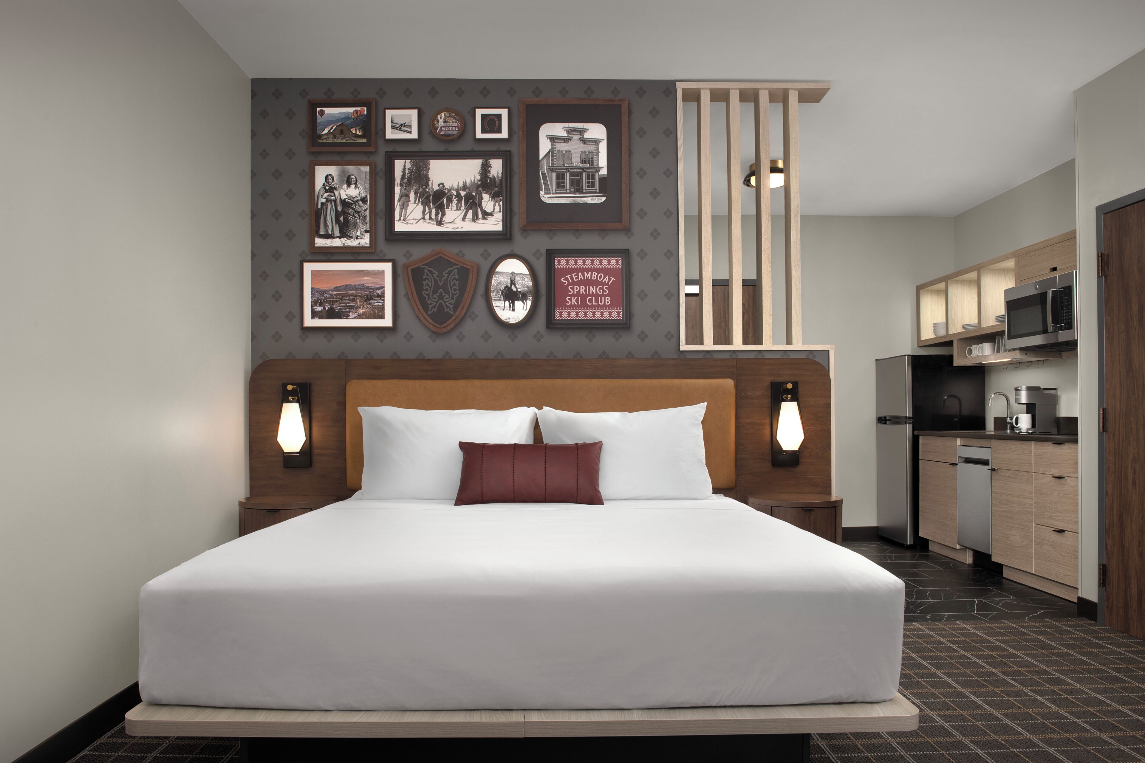 Habitación de hotel con una cama grande, un televisor montado en la pared, una zona de cocina y cuadros enmarcados.