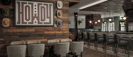 A modern restaurant with a wooden wall, a large framed artwork, and a bar area with stools.