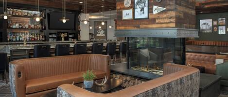 A bar area with a wooden ceiling, bar stools, and a television. There is a seating area with a sofa and a fireplace.