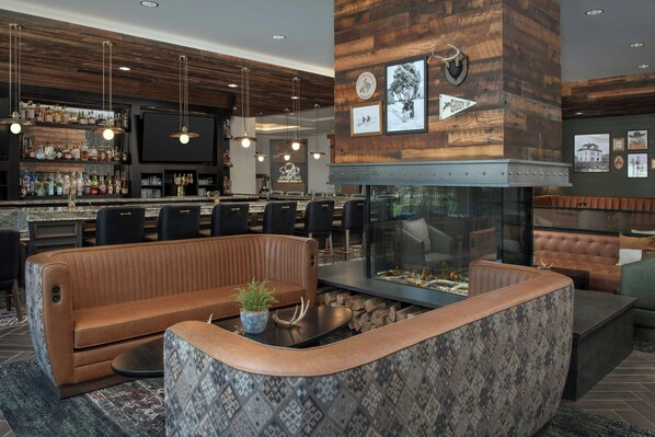 A bar area with a wooden ceiling, bar stools, and a television. There is a seating area with a sofa and a fireplace.