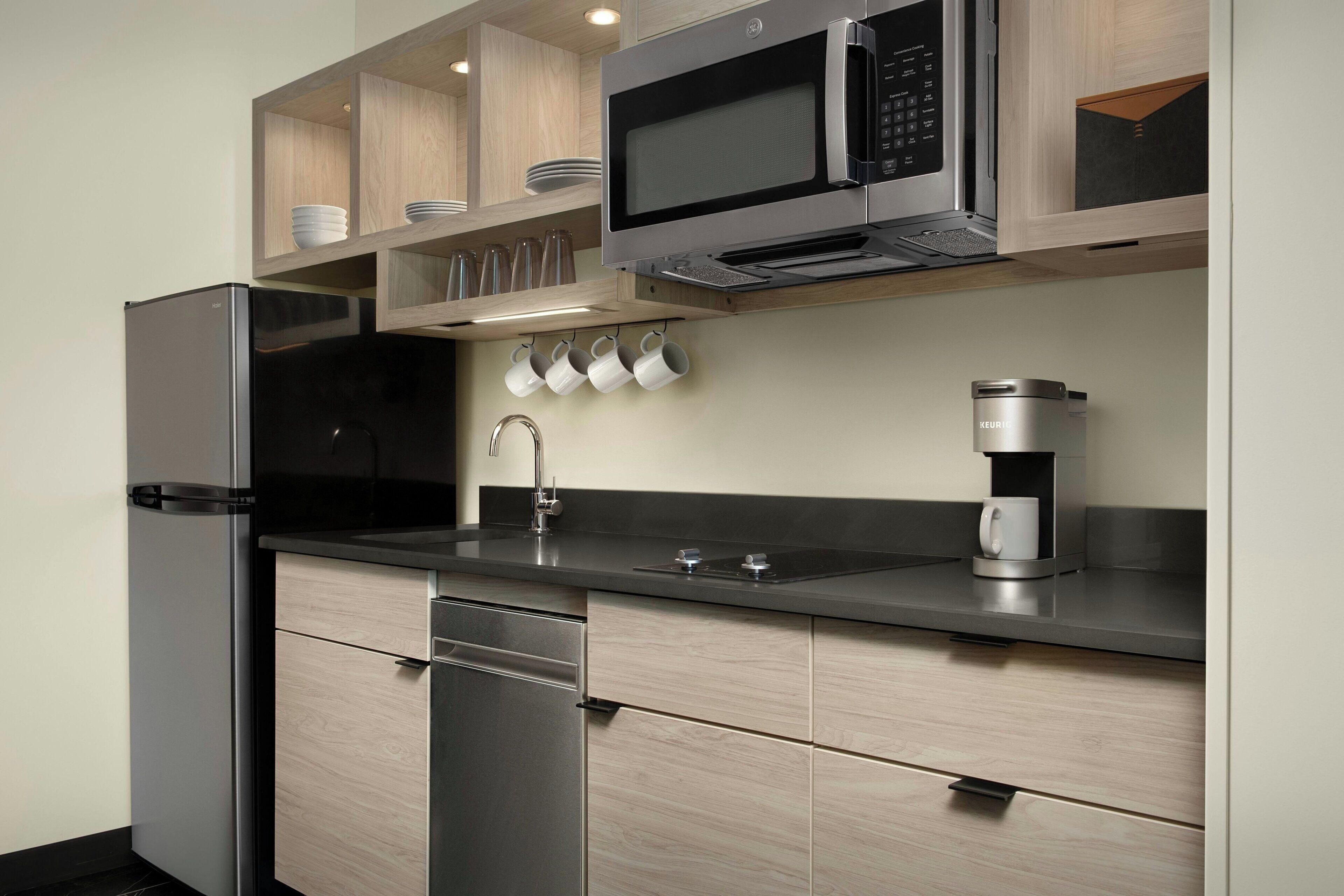Una cocina moderna con refrigerador, microondas, cafetera y armarios de madera.