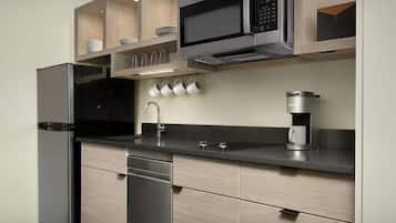 Una cocina moderna con refrigerador, microondas, cafetera y armarios de madera.