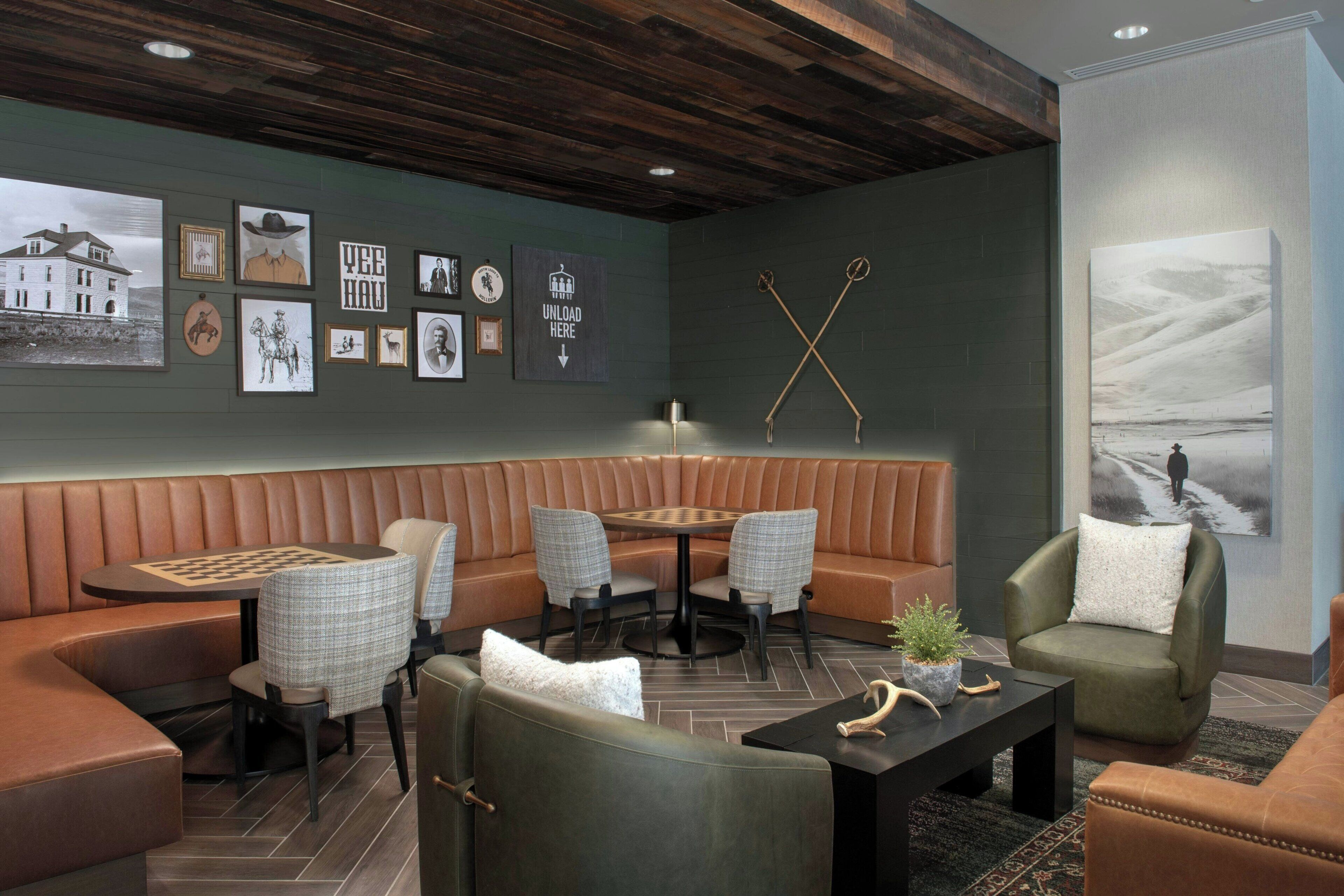 Un espacio lounge moderno con una banqueta de cuero, una mesa de ajedrez y obras de arte colgadas en la pared.