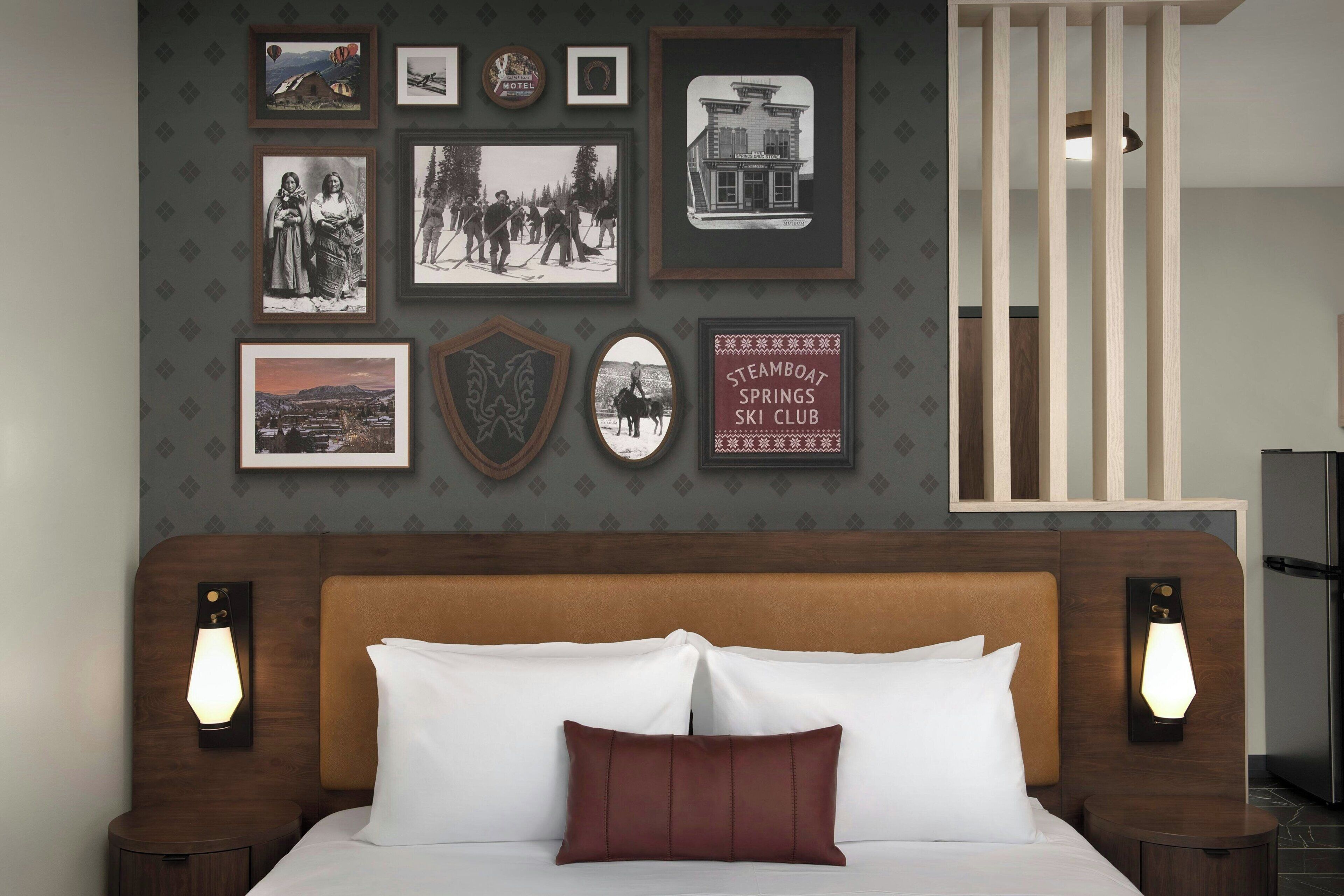 Habitación de hotel con cama, cuadros en la pared y cabecera.