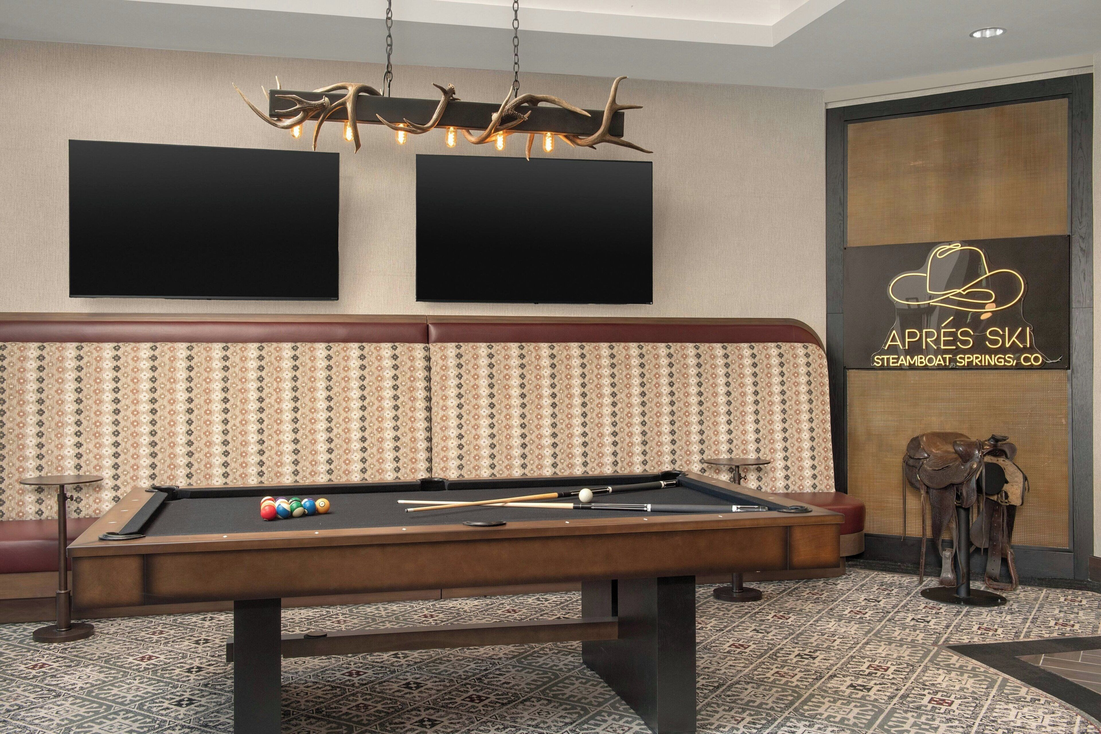 A pool table with balls, a pool cue, and a billiard rack. There is a patterned wall behind the table and a decorative light fixture above it.