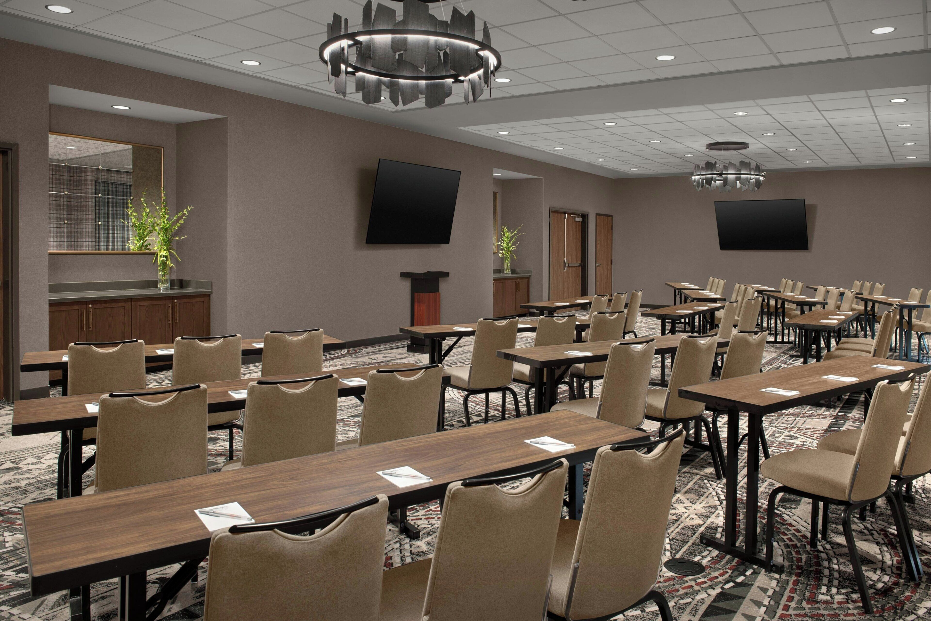 A conference room with multiple tables and chairs, a large flat-screen TV, and a decorative chandelier.
