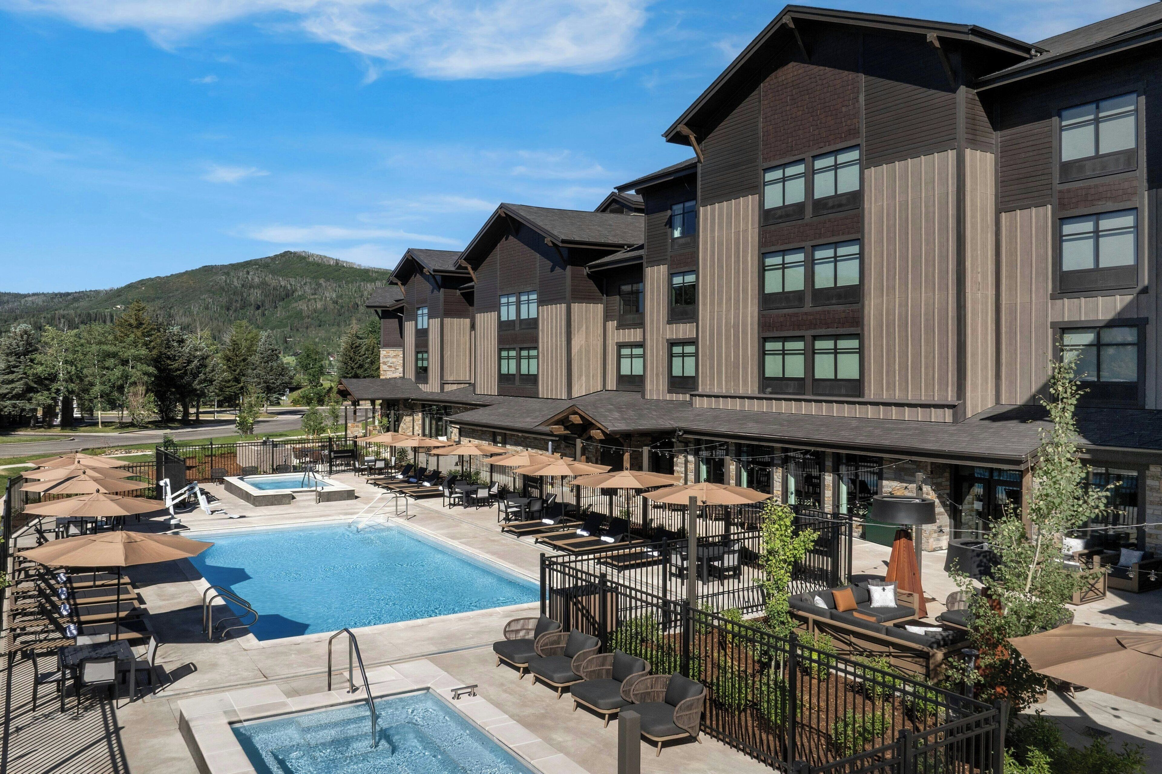 A hotel with a swimming pool, outdoor seating, and a mountain backdrop.