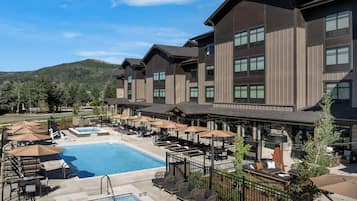 A hotel with a swimming pool, outdoor seating, and a mountain backdrop.