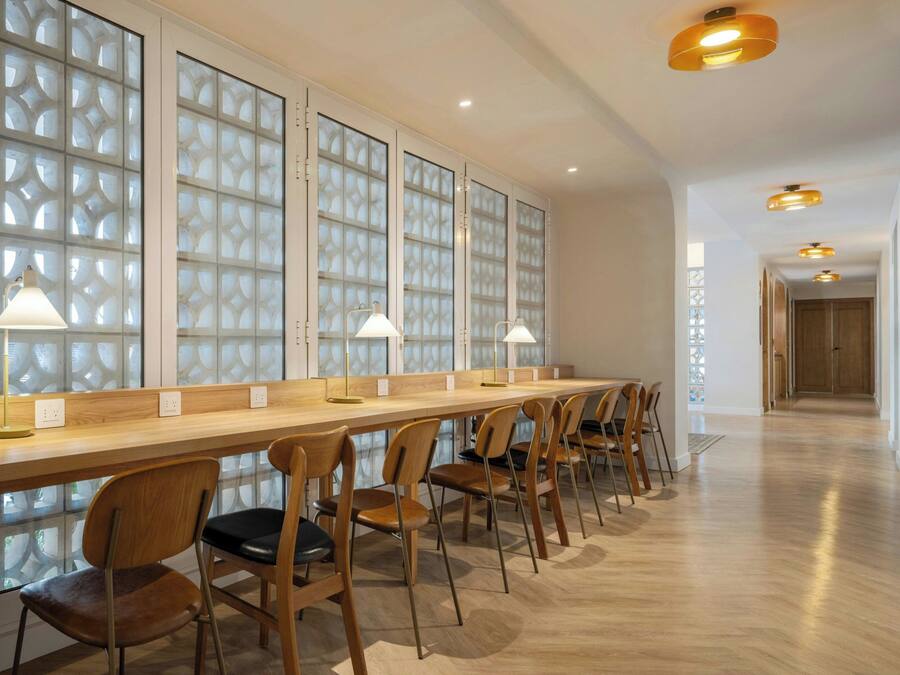 A long, wooden reception desk with chairs, a patterned glass partition, and pendant lighting.