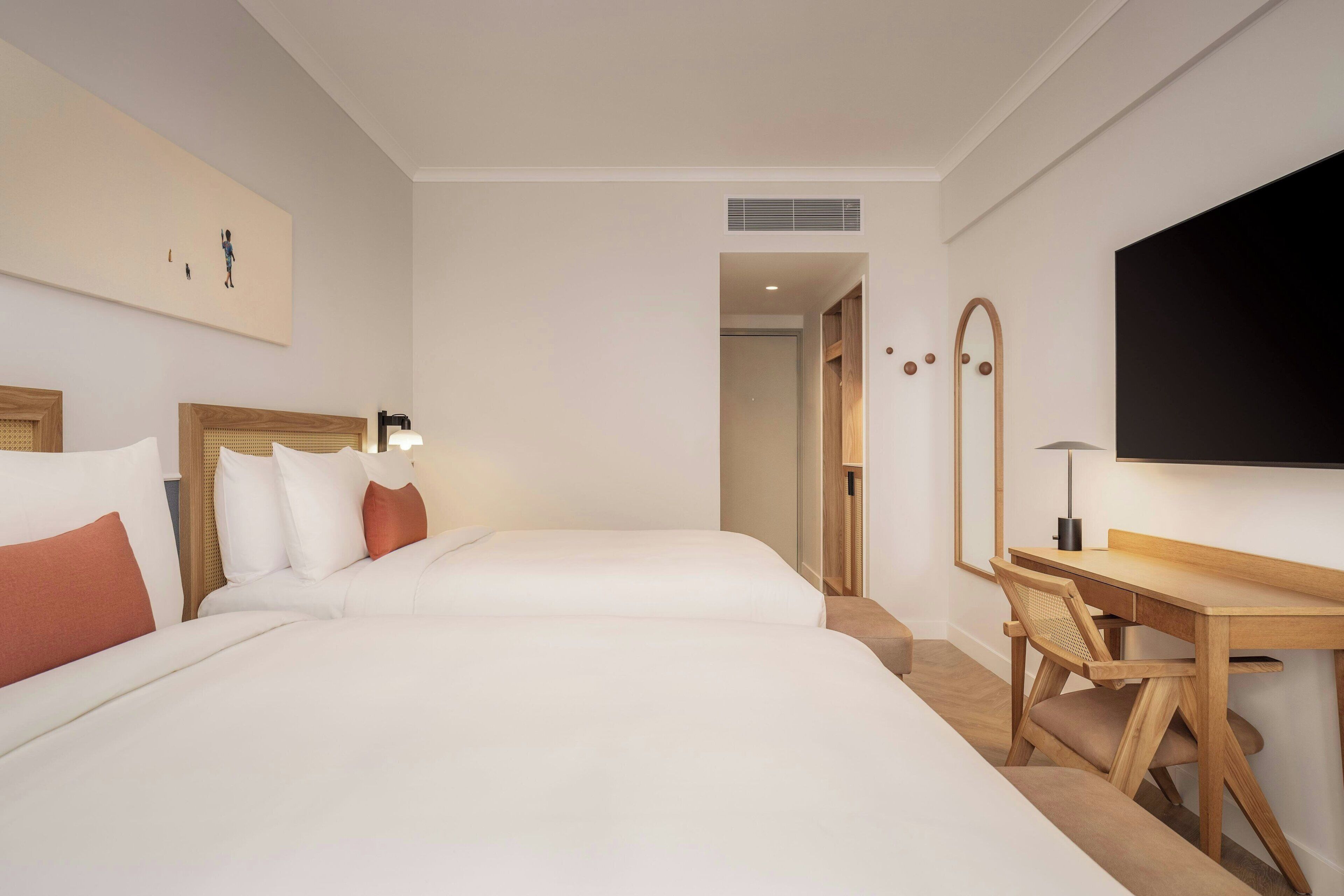 Une chambre d’hôtel avec deux lits, un bureau, un miroir et une télévision.