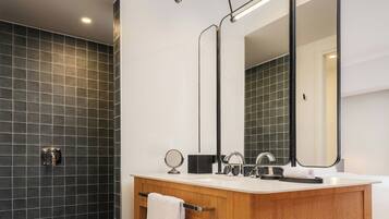 Une salle de bain moderne avec un mur recouvert de carreaux foncés, un meuble-lavabo en bois, un miroir et un porte-serviettes.
