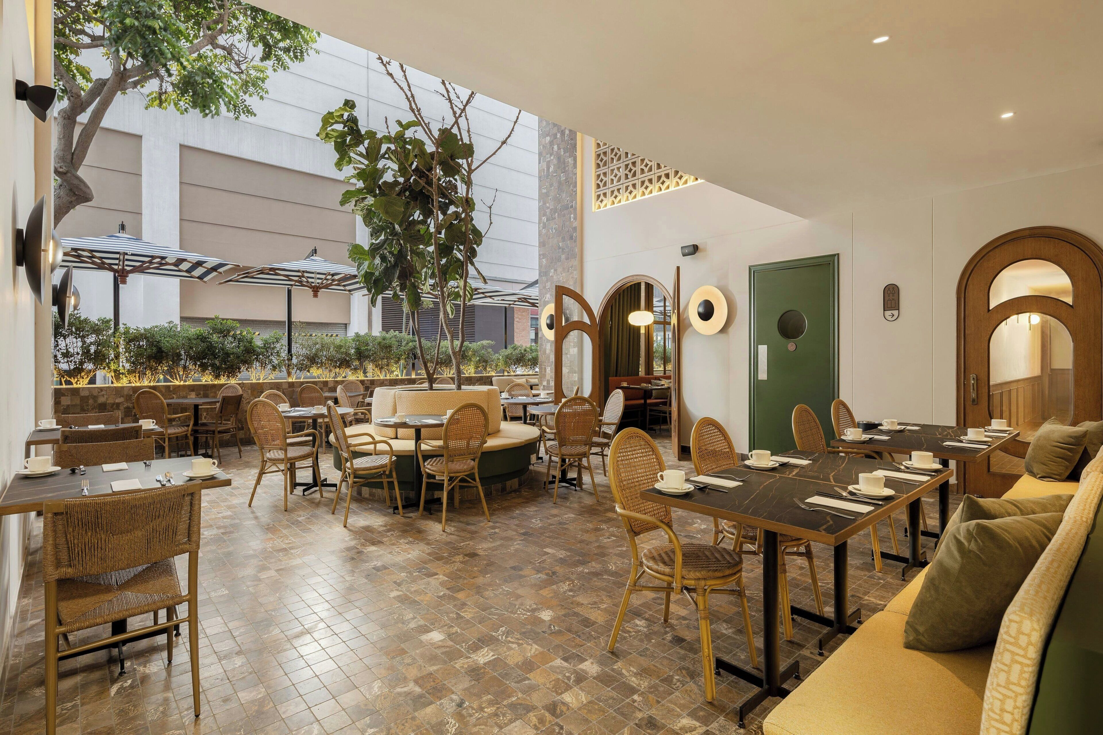Un restaurante con terraza, mesas, sillas y una puerta verde.