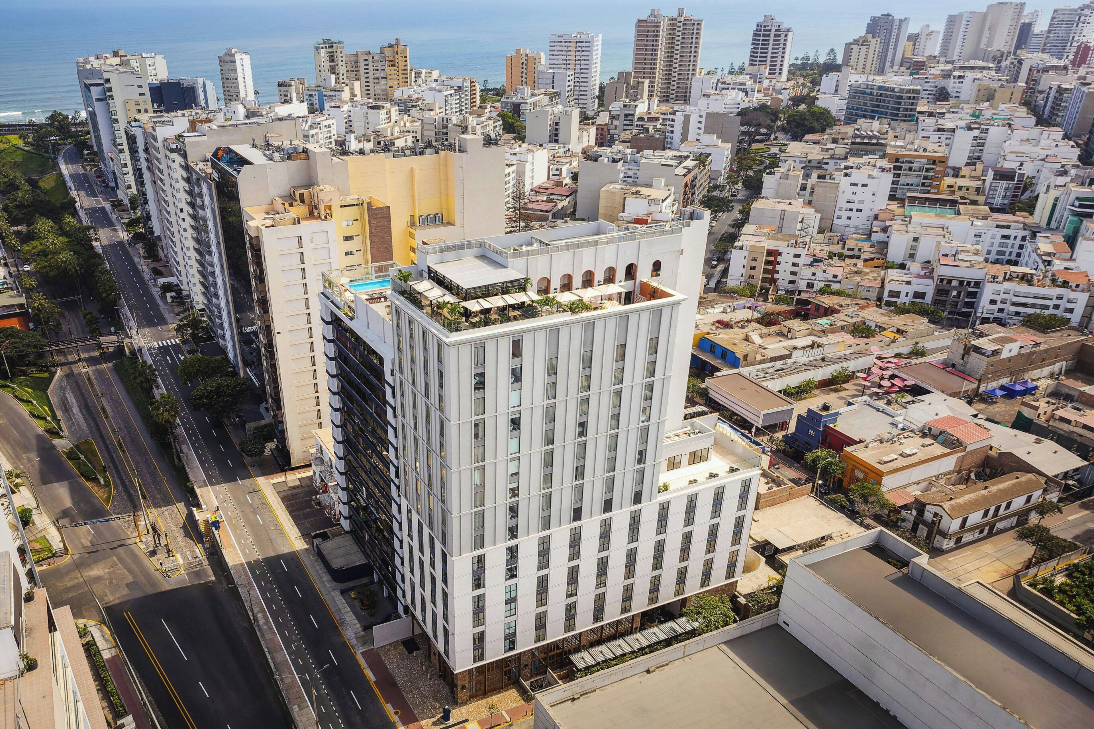 Un edificio de gran altura con varios pisos, una terraza en la azotea con asientos al aire libre y vistas de la ciudad circundante.