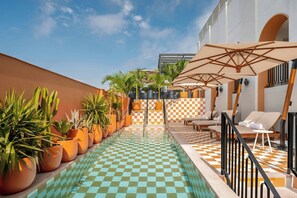 A pool area with checkered tiles, lounge chairs, and potted plants.