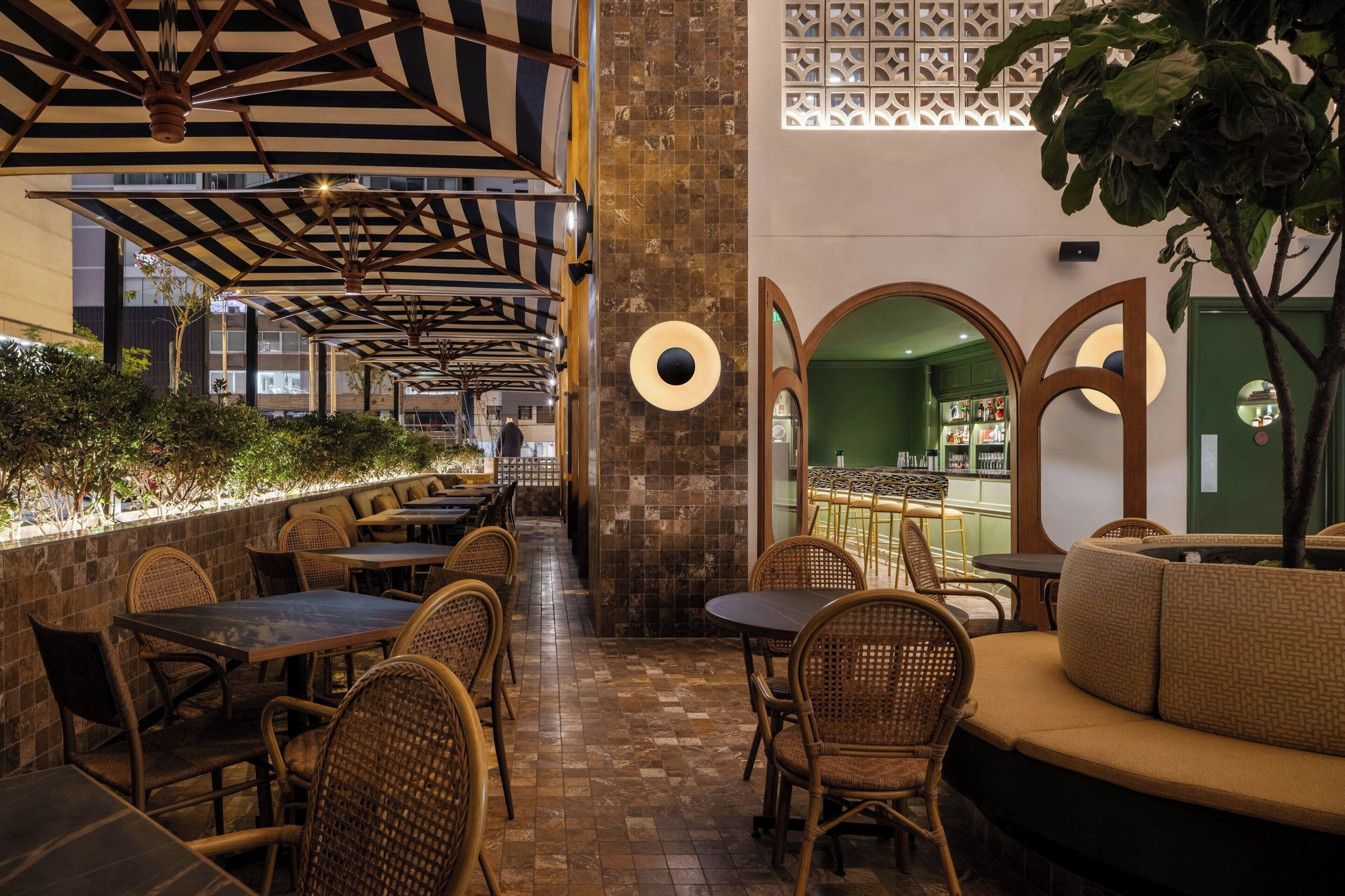 Un espacio al aire libre con mesas y sillas, una pared decorativa con un diseño circular y vistas a una zona de bar.