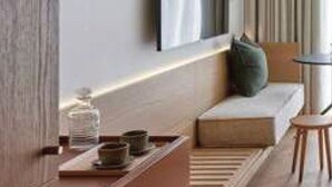 Een moderne hotelkamer met een minimalistisch design, voorzien van een bank, een kleine tafel en een flatscreen televisie aan de muur.