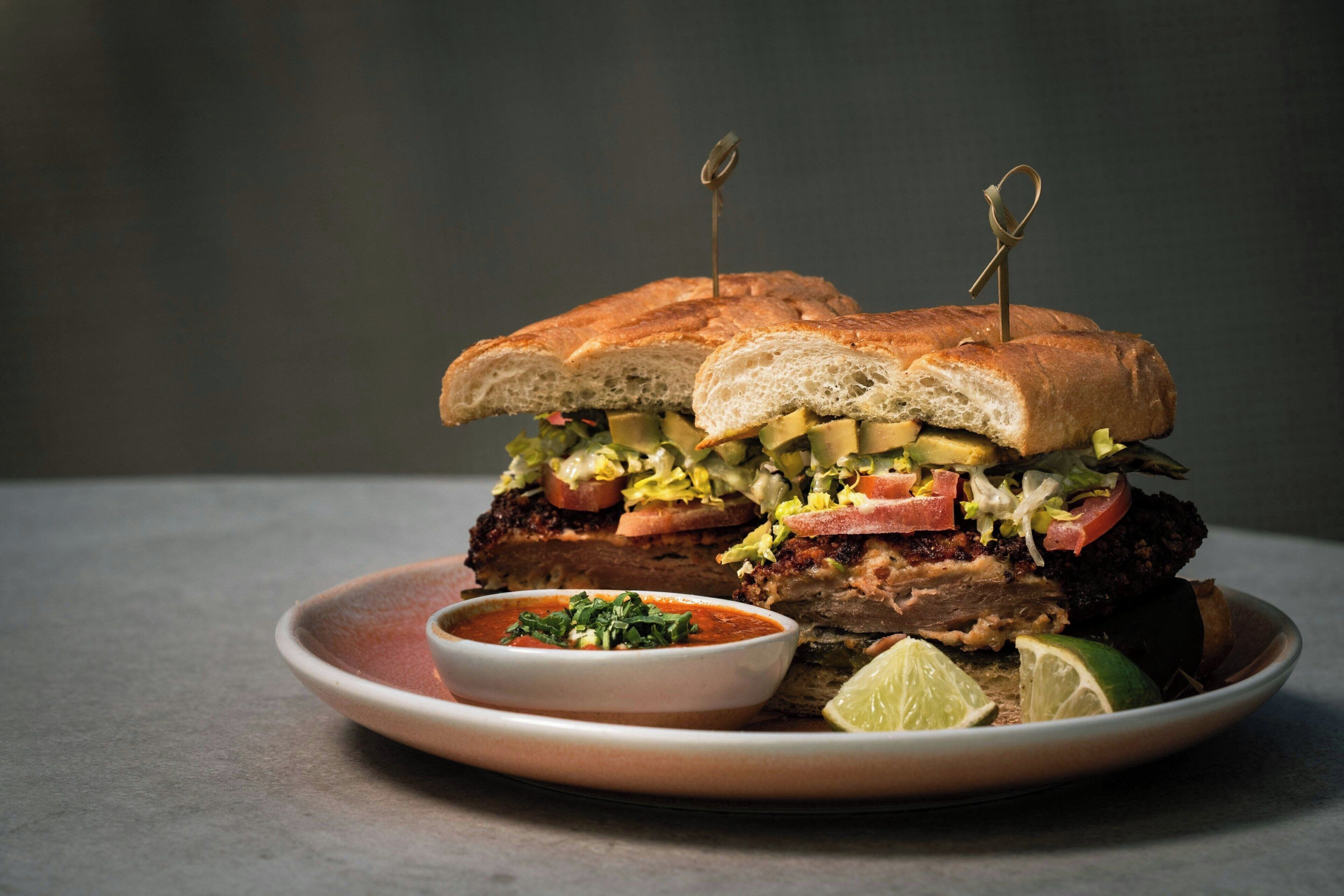 A sandwich with a side of sauce and lime wedges on a plate.