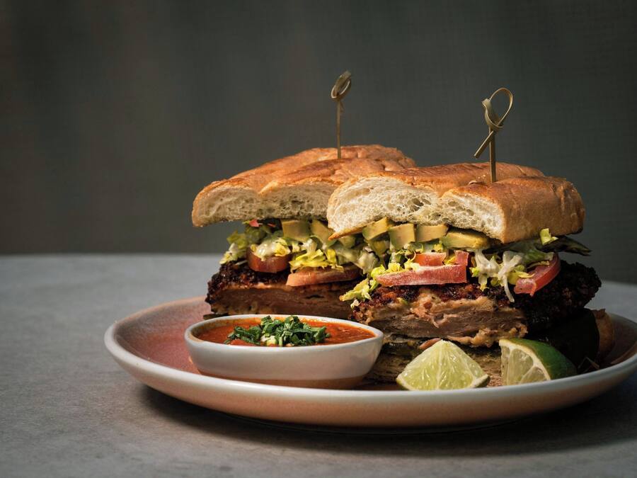 A sandwich with a side of sauce and lime wedges on a plate.