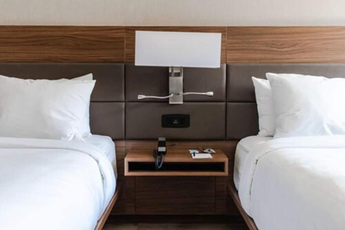 Une chambre d’hôtel avec deux lits, une table de chevet avec une lampe et un panneau de commande fixé au mur.
