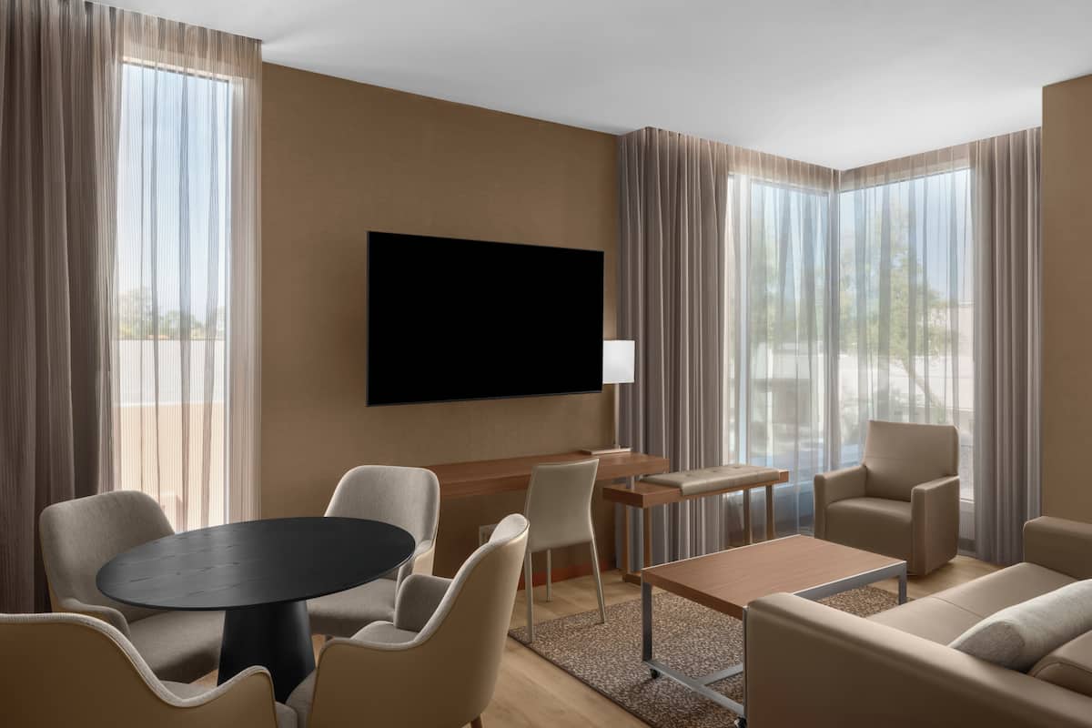 Une chambre d’hôtel moderne équipée d’un téléviseur à écran plat, d’une table de salle à manger ronde, d’un canapé et d’un fauteuil.