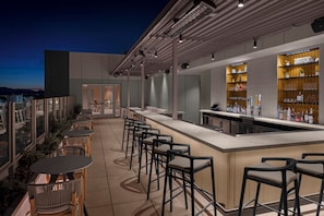 A rooftop bar with a long counter, multiple bar stools, and a view of the cityscape. - AC Hotel By Marriott Scottsdale Old Town (Scottsdale)
