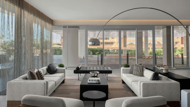 Una sala de estar moderna con dos sofás, una mesa de centro y un ventanal con vistas a un edificio y zonas verdes.